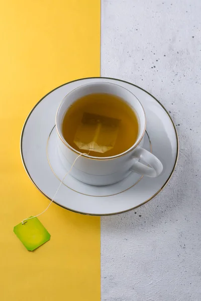 cup of tea with tea bag on bright yellow and white textured background, bi colored or two colored background, mock up, top view