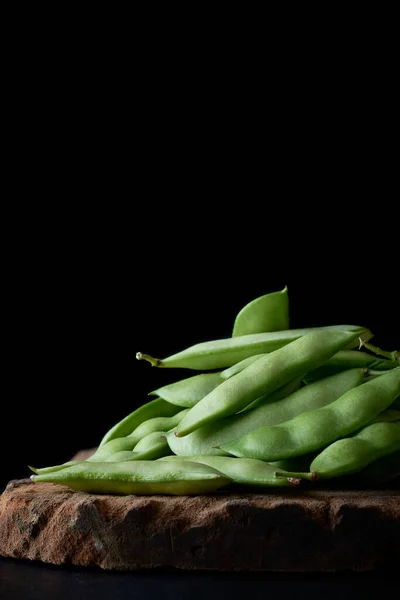 ボード上のエンドウ豆のポッドの山 その栄養価の高い種子やポッドのために広く栽培されているマメ科植物の種類 コピースペースと黒の背景に隔離された新鮮な収穫野菜 選択的な焦点 — ストック写真
