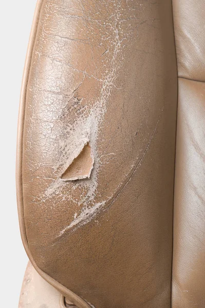 close-up section of used worn and torn leather car seat, beige color seat with wear and tear, including scuffs, creases and scratches, repair and services in leather upholstery restoration concept