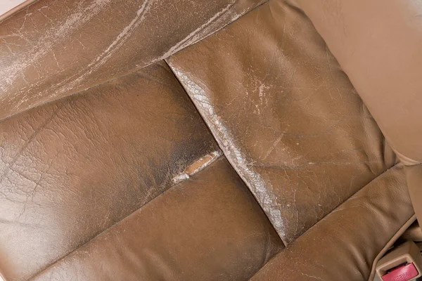 close-up of used worn and torn leather car seat, beige seat with wear and tear, including scuffs, creases and scratches, repair and services in leather upholstery restoration concept, space for text