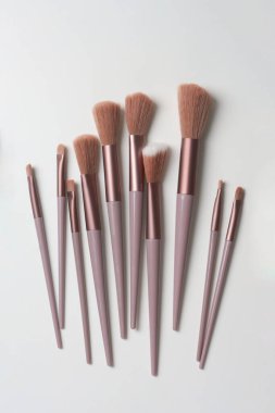 Beyaz masa yüzeyine saçılmış makyaj fırçaları, belirli amaçlar için tasarlanmış temel kozmetik araçlarının çeşitli şekilleri ve boyutları, doğrudan yukarıdan kopyalanmış