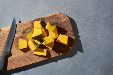 Tahta kesme tahtasının üzerinde balkabağı dilimleri mutfak masasının üstünde bıçakla pişirilmiş sebze parçaları, yukarıdan kopyalanmış uzay ile alınmış.