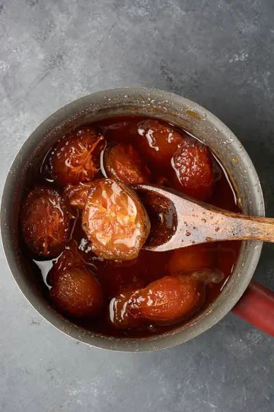 ambarella or june plum jam or marmalade in pan with wooden spoon, tropical sweet flavored juicy dessert on table top, taken from above with copy space