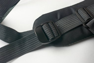 Beyaz yüzey arka planında, kaydırma ayarlayıcısı ile tutturulmuş plastik tokalı, örülmüş kumaştan yapılmış, siyah sırt çantasından omuz askısı.