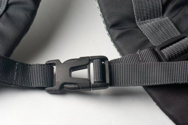 Beyaz yüzey arkaplanındaki sırt çantasına siyah plastik toka iliştirilmiş.