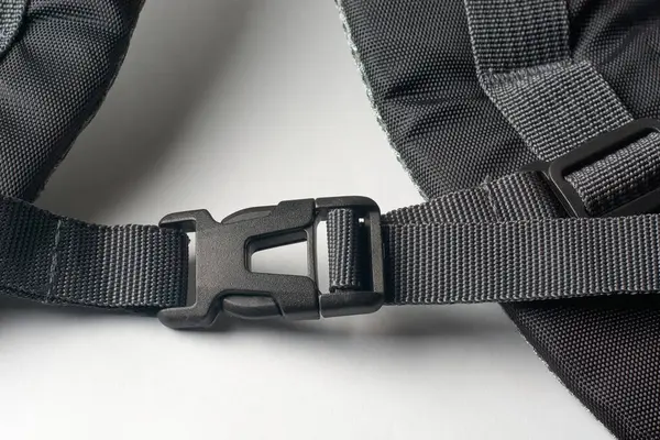 Beyaz yüzey arkaplanındaki sırt çantasına siyah plastik toka iliştirilmiş.