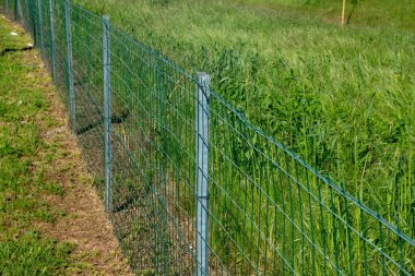 Galvanize çelik direkli ve elektro kaynaklı dikdörtgen örgülü bir alanda çit. Mülk sınırları sırık ve ağlarla sınırlandırılır.