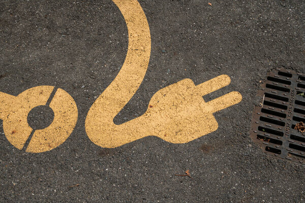 Электромобили, зарядное устройство обозначаются символом автомобиля и кабелем зарядки. Место зарезервировано для электрической зарядки, символ на тротуаре автостоянок на улицах города. устойчивая мобильность и зеленые инновации будущее. новости