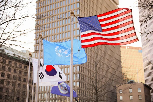 The US flag represents democracy, freedom, and patriotism. The UN flag symbolizes global cooperation and peace. The Korean flag symbolizes balance, harmony, and unity.