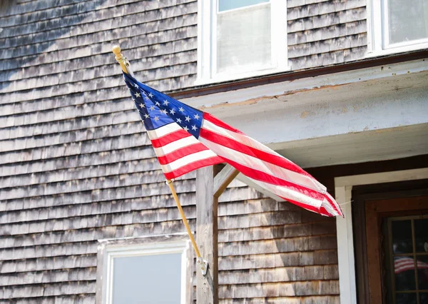stock image US flag proudly displayed in front of an American house symbolizes patriotism, national identity, and love for one's country. It represents unity, freedom, and the values upon which the United States was built