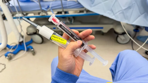 白い背景の血液のための青い液体が付いている注射器を握る手 — ストック写真