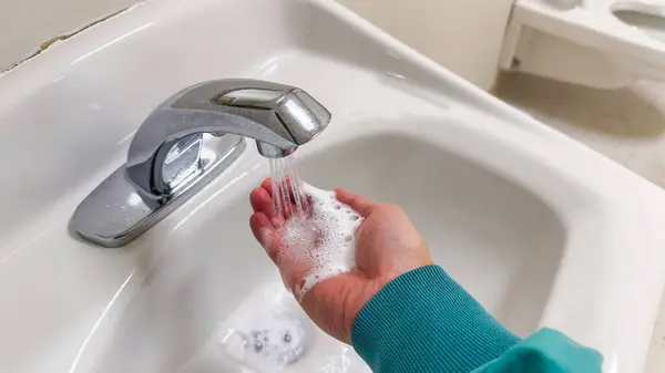 woman washing hands with soap and faucet in bathroom.