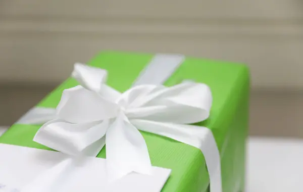 a white box with a gift on a green bow on a white background.