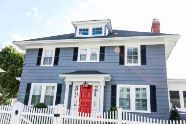 Kırmızı tuğlalı ve mavi verandalı beyaz ahşap ev.