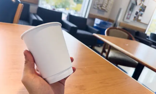 disposable coffee cup in hand on wooden table