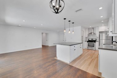 Büyük beyaz mutfağı ve ahşap zeminli yemek masası olan modern bir daire.