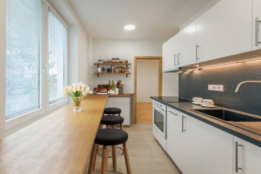 Beyaz duvarları, ahşap zemini ve geniş penceresi olan modern mutfak..