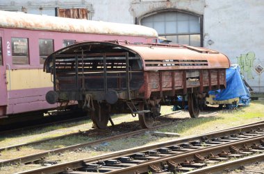 Endüstriyel bir vagonun arka planında eski bir tren lokomotifi, tren istasyonu, açık bir alanda raylar.,