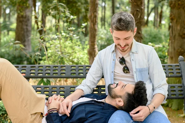 年轻的同性恋男子在公园里快乐地望着彼此的时候 双膝跪在长椅上冷冰冰的 — 图库照片