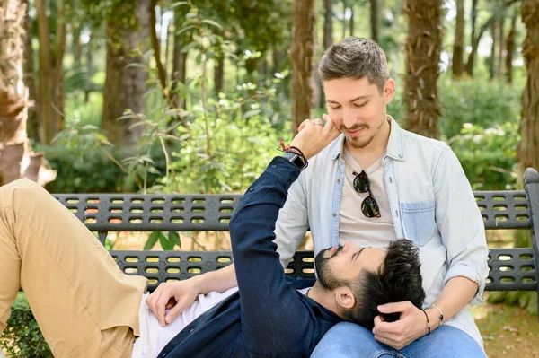 盖伊把头靠在男朋友的膝上 轻轻地摸着脸颊 在公园的长椅上休息 相互望着对方 — 图库照片