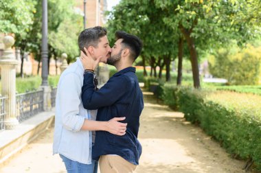 Homoseksüel eşcinsel çiftin güneşli parkta sarılıp öpüşmelerinin yan görüntüsü.