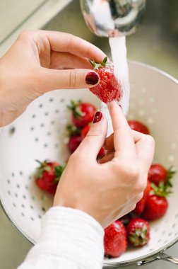 Anonim bir kadının yüksek açılı görüntüsü leziz taze çilek gösterisi yaparken lavaboda sağlıklı böğürtlenleri mutfakta suyla yıkıyor.