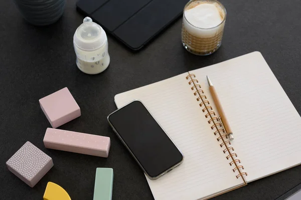 高角的打开的笔记本 装有笔和杯咖啡 放在智能手机旁边 屏幕上有黑色 桌上有各种玩具旁边有一瓶牛奶 — 图库照片
