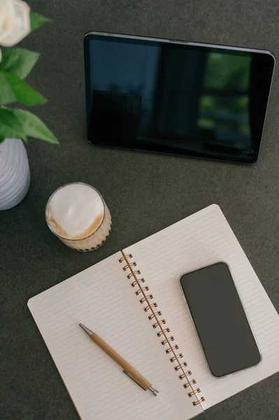 在智能手机上方 笔架在打开的螺旋式笔记本上 旁边是一杯美味的卡布奇诺咖啡和办公室的餐桌 — 图库照片