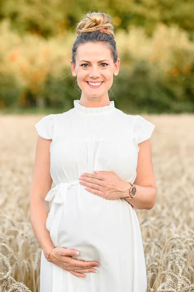 积极的年轻女性 身穿白衣 面带微笑 看着相机 站在田里 用干草 用双手触摸模糊的大自然 — 图库照片