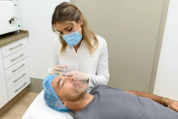 Tıbbi Maskeli Kadın Kozmetik Uzmanı Estetik Kliniğinde Yatakta Yatan Erkek — Stok fotoğraf