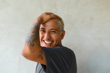 Siyah gömlekli, pozitif, genç, latin bir erkek. Gri arka planda dikilirken gülümsüyor ve kameraya bakıyor.