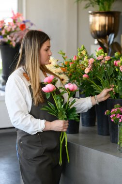 Önlüklü genç bayan çiçekçi çiçek dükkanında sergilenen vazolara taze gül buketi yerleştiriyor.