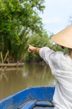 Vietnam 'da Mekong Deltası' nda turne sırasında ağaçlara işaret eden günlük giysiler içinde Vietnamlı bir şapka takan Kafkas genç sarışın turistin arka görüntüsü. Yüksek kalite fotoğraf