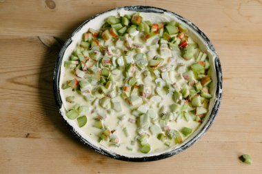 Pişmemiş turta hamuruyla tavanın en üst görüntüsü sosa batırılmış ve yüzeye yerleştirilmiş yeşil ravent sapları.