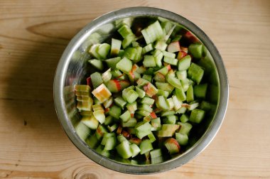 Kabuğun üst görüntüsü, kabuğu soyulmuş çiğ çiğ çiğ çiğ çiğ rubarb küçük parçalara bölünmüş ve gün ışığında ahşap masaya yerleştirilmiş.