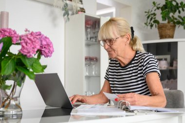 Yaratıcı çalışma alanında çalışırken, dizüstü bilgisayarda yazan günlük giysiler ve gözlüklerle serbest çalışan genç bir kadın.