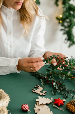 İsimsiz kadın dekorasyonundan ve elinde kırmızı böğürtlenli yeşil dallarla Noel çelengi tutmaktan farklı çelenklerin yanında yeşil arka plan, el işi eşyalar. Noel konsepti