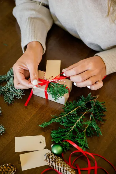 Noel hediyelerini süveter ile paketleyen bir avuç kadın kağıt, makas, renkli kurdeleler kullanıyor ve evdeki kutuya köknar koyuyor. Arka plan ışıklarında. Noel konsepti