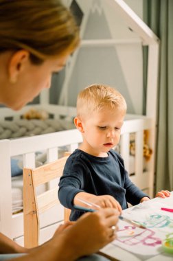 Sarışın, tatlı, yoğun bir çocuk, sıradan görünümlü, uzun saçlı bir anne, masada oturuyor ve gün boyunca resimlerini kağıda çiziyor. Kadın evde çocuk eğitiyor.