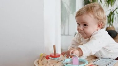 Küçük beyaz kız yürümeyi öğreniyor, destek olarak bir tahta oyun masasını itiyor, kameraya gülümsüyor. çocukluk ve aile kavramı