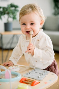 Şirin, küçük bir kız, rahat kıyafetler giymiş, tahta oyuncaklarla oynuyor, kameraya bakıyor, dişlek bir gülümsemeyle gülüyor, bir yaşında, ilk adımları. çocukluk kavramı
