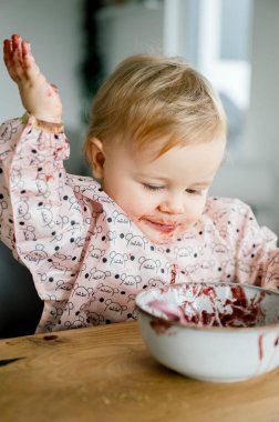 Gülümseyen bebek oturma odasındaki yüksek sandalyede tek başına püre yiyor. Sevimli küçük çocuk kavanozdan meyve ya da sebze püresi alıyor. Bebeklik, çocukluk kavramı.