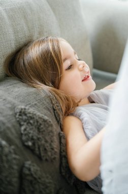 Kitapta kaybolmuş genç bir kız, rahat bir şekilde koltukta uzanıyor, okunacak sessiz bir anın tadını çıkarıyor, kanepeye yaslanıyor, çocuk ve aile kavramı.