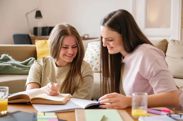 female students in t-shirt and jeans, long hair sitting in living room, on the table books, note pad, glass orange juice, learning for exam, laughing in an apartment in Eastern Europe, Budapest