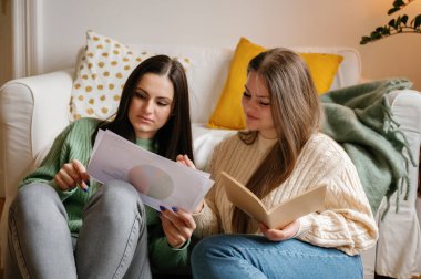 Odaklanmış genç bir kadın, arkadaşıyla birlikte bir belgeyi gözden geçirir. İkisi de koltuğun önünde rahatça otururlar. Bitkilerle samimi bir arka plan, yumuşak ışık, Budapeşte 'de bir daire