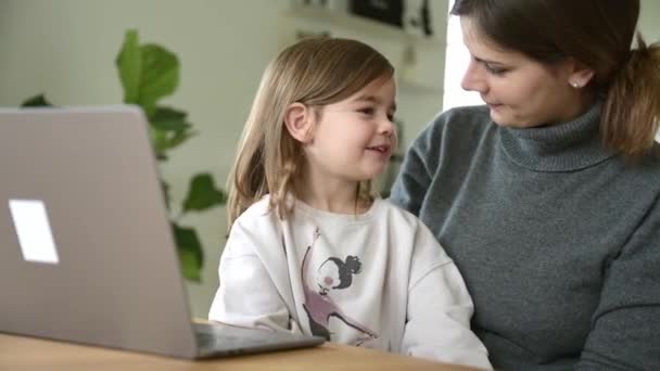 在家里的办公室里 一个母亲和一个小女孩坐在桌旁 年轻的女性在笔记本电脑上工作 而她的女儿则在旁边玩耍 她把工作和家庭生活 混合办公室和工作生活的平衡混合在一起 — 图库视频影像