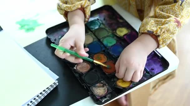 絵筆を手に持っている認識できない幼い子供は 鮮やかな色とアートワークに焦点を当てた水彩画 子供の絵画の手の作物 — ストック動画