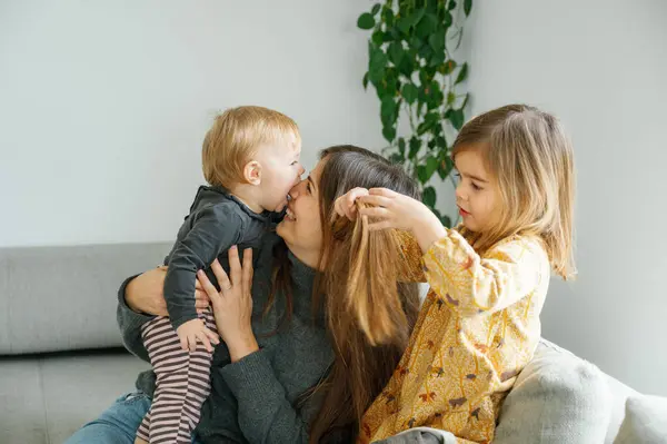 Samimi bir an, mutlu ve genç bir annenin gülüşünü yakalar. Yavrusu neşeyle yüzünü yalarken, büyük kardeş eğlence, kopyalama alanı, aile kavramına katılır.