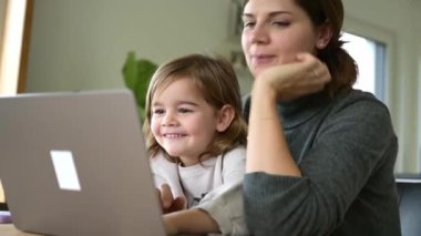 Küçük tatlı kız evde annesiyle birlikte dizüstü bilgisayar kullanmaktan hoşlanıyor. Kafkasyalı küçük kız annesiyle birlikte bilgisayardan internet tarayıcı kullanarak internetten öğreniyor. Çocuk eğitimi konsepti