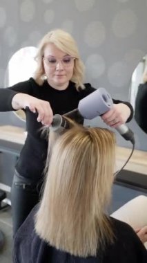Kuaförde çalışan genç bir kuaför, kuaför elleri saç fırçalama makinesine uzun sarı saç teli uzatıyor. Kuafördeki genç ve güzel kadın, küçük iş konsepti.